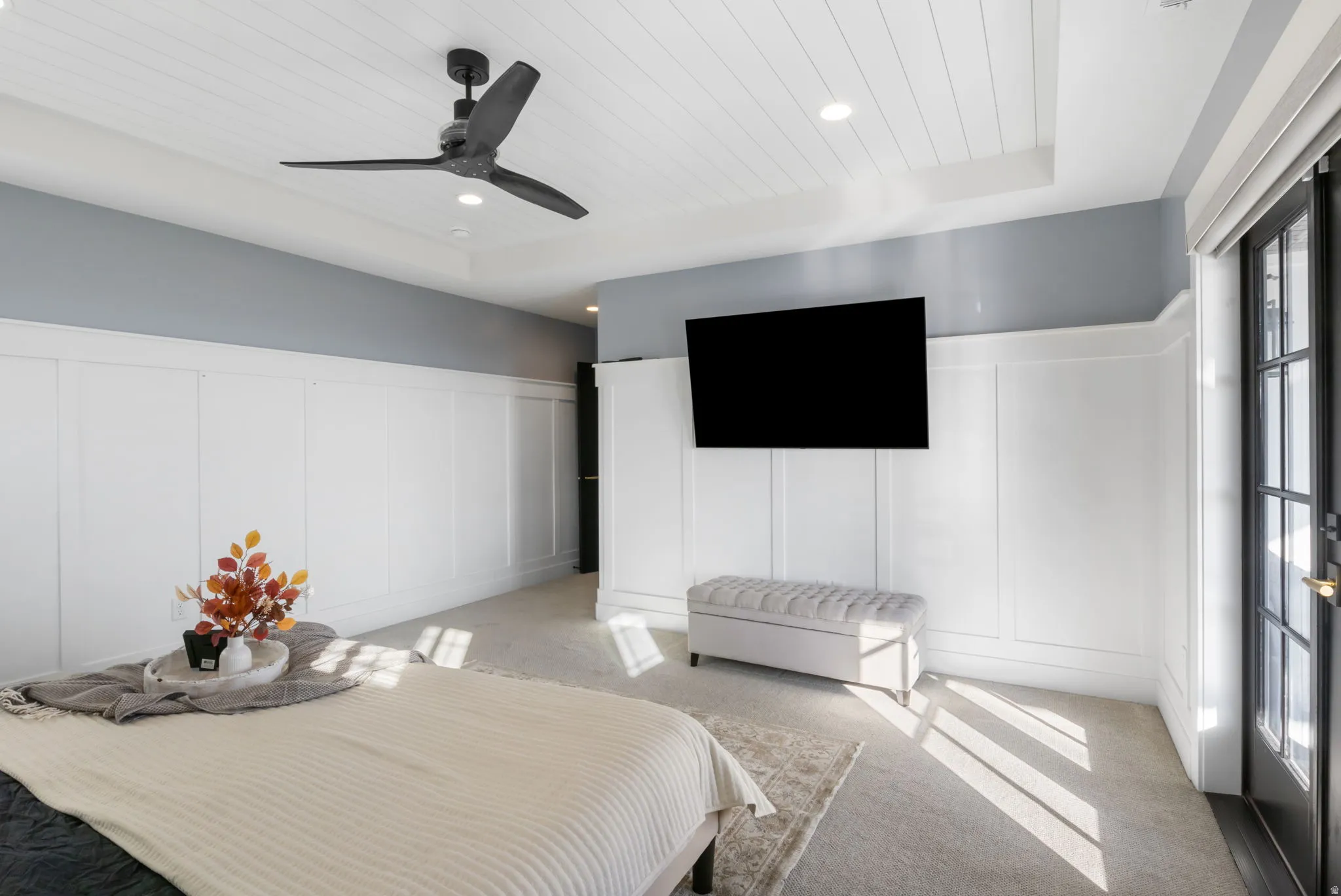 Carpeted bedroom with a decorative wall, a wainscoted wall, wood ceiling, and a ceiling fan