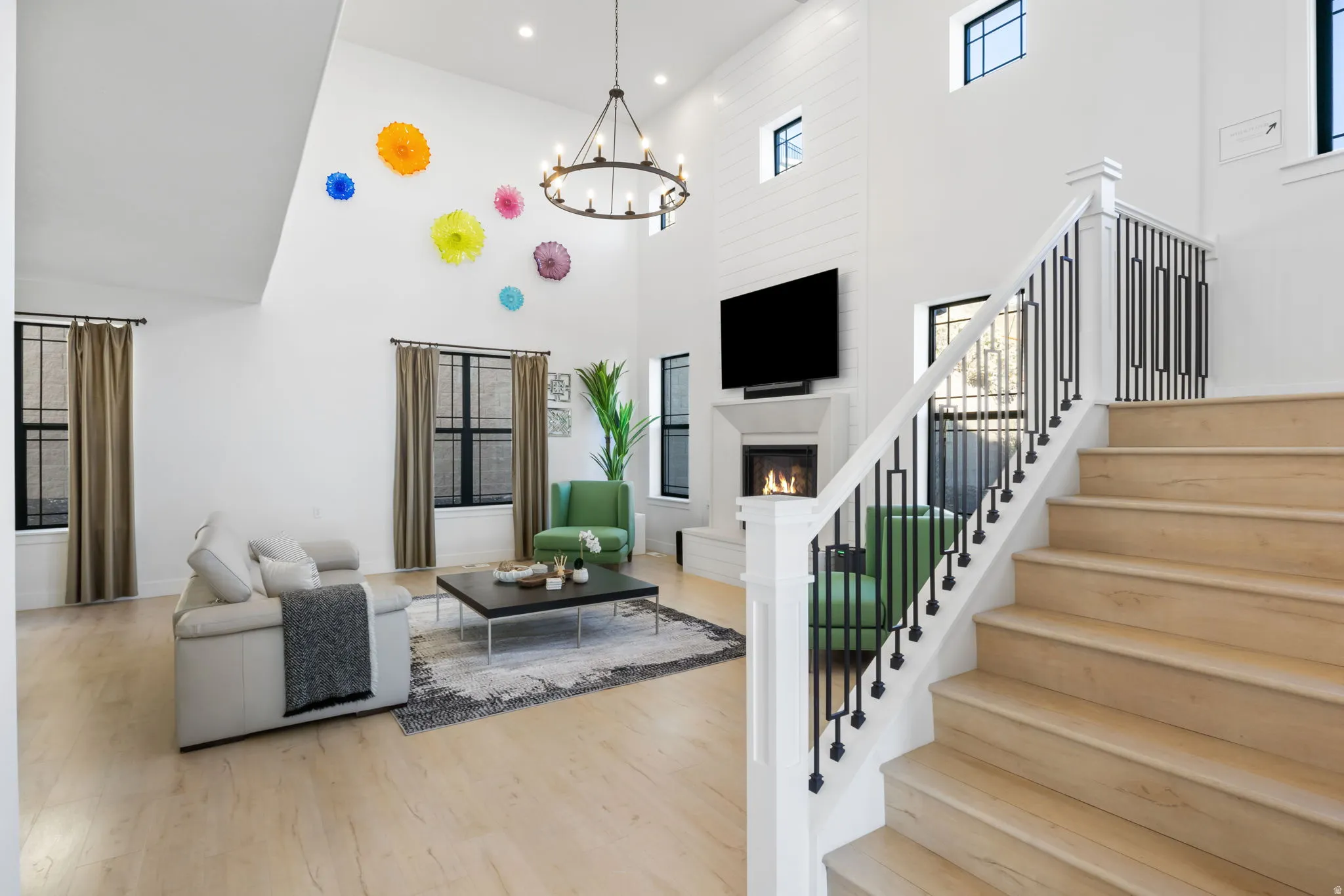 Living area featuring a warm lit fireplace, stairs, recessed lighting, light wood-style floors, and a high ceiling