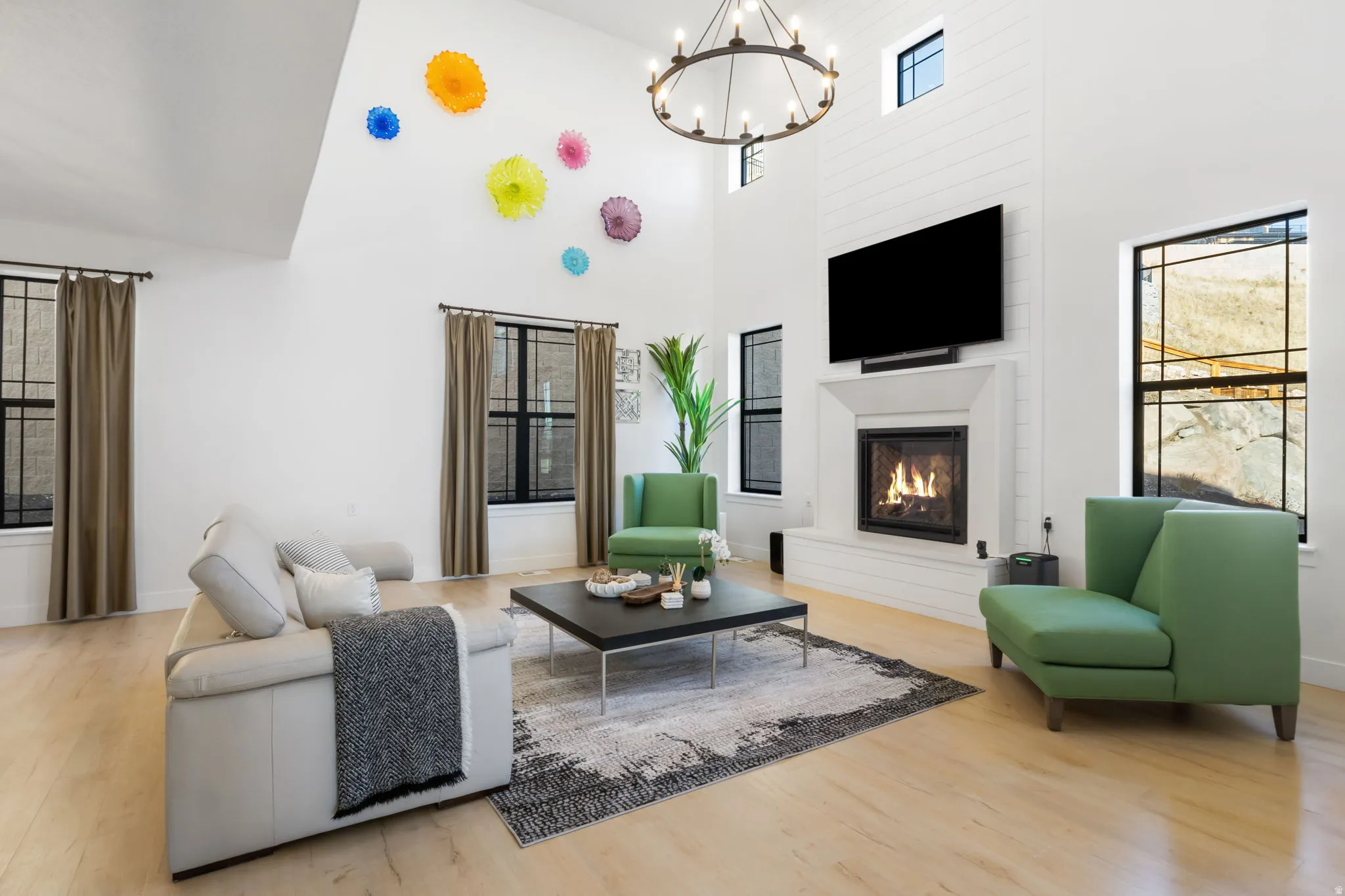 Living room featuring a towering ceiling, healthy amount of natural light, a glass covered fireplace, and light wood-style flooring
