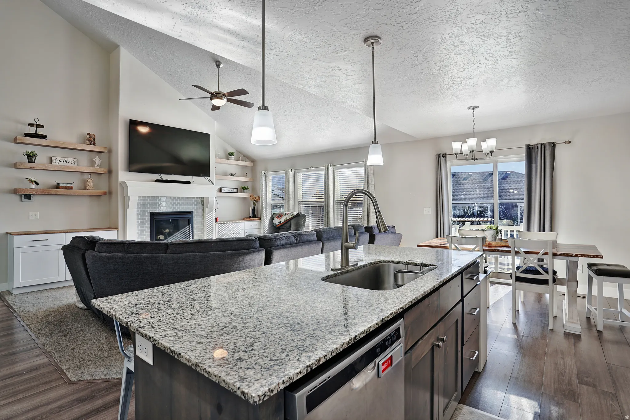 Kitchen featuring lofted ceiling, light stone countertops, dark wood finished floors, dishwasher, and a glass covered fireplace