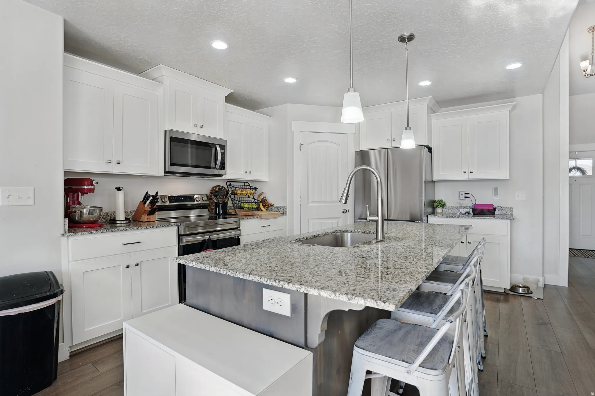 Kitchen featuring white cabinets, light stone countertops, appliances with stainless steel finishes, dark wood-style floors, and recessed lighting