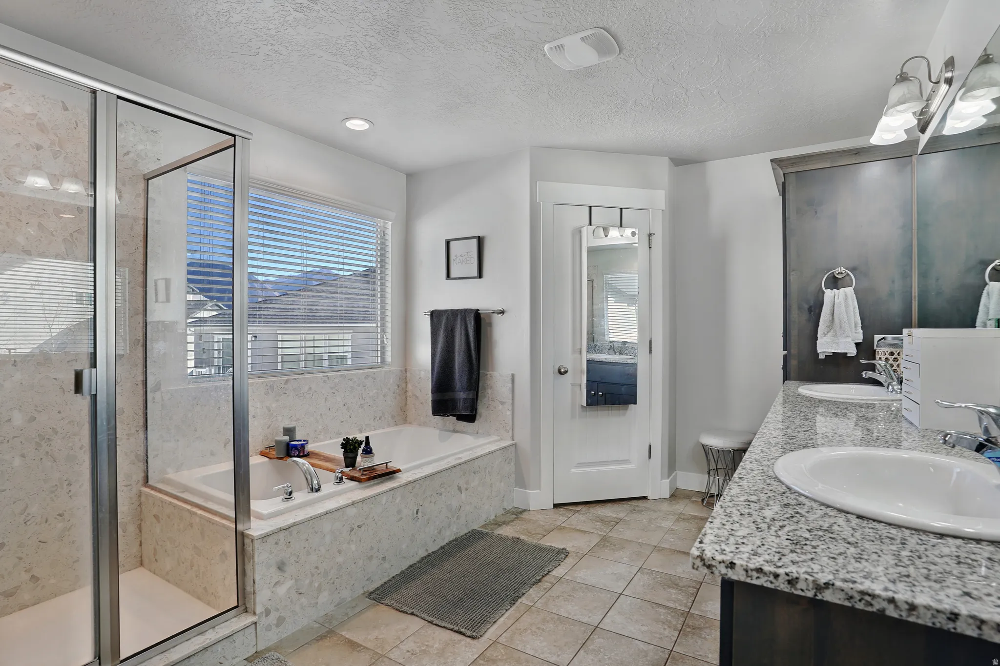 Bathroom with double vanity, a stall shower, a textured ceiling, a bath, and light tile patterned floors