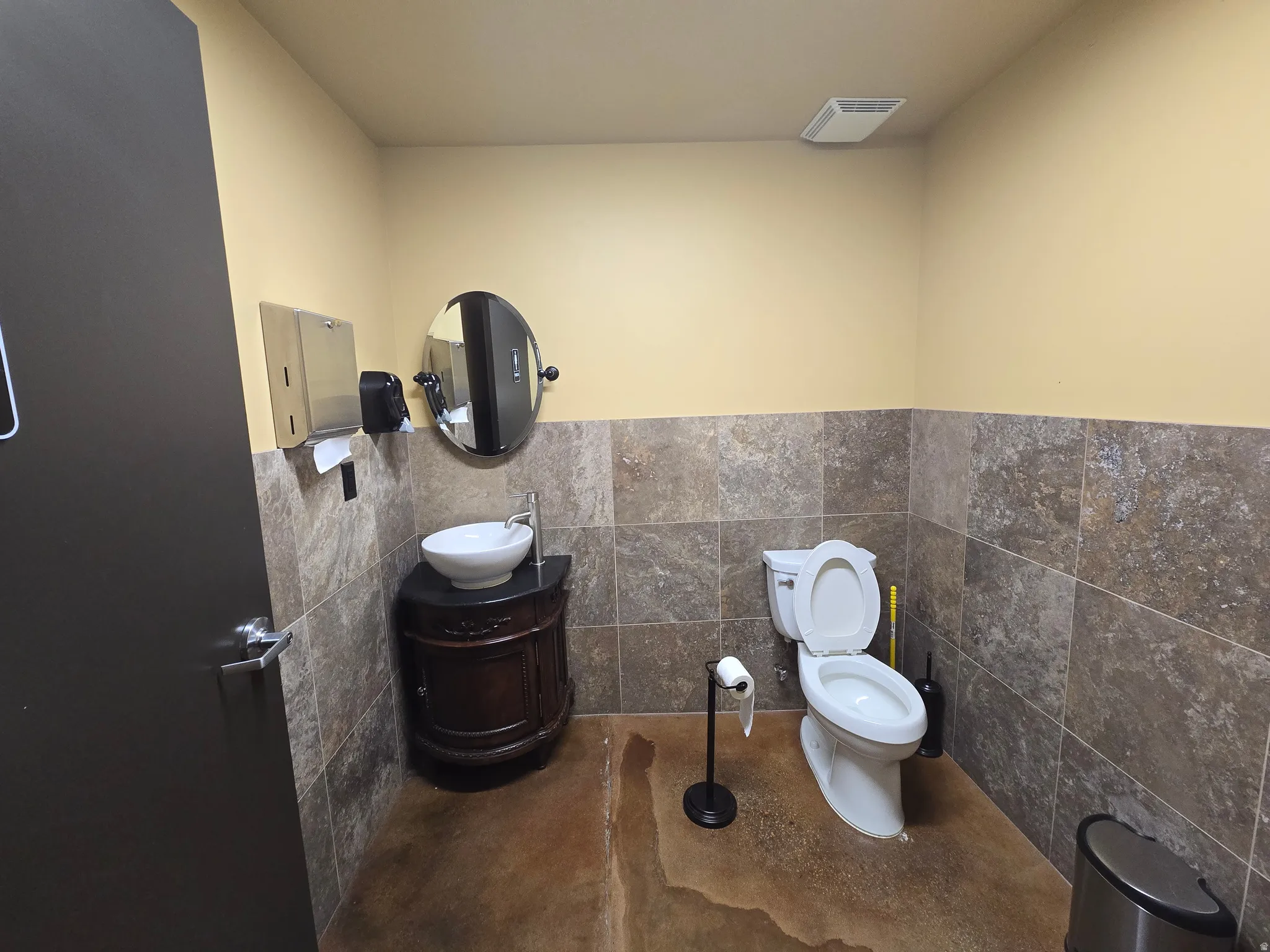 Half bathroom featuring tile walls, vanity, wainscoting, and concrete flooring