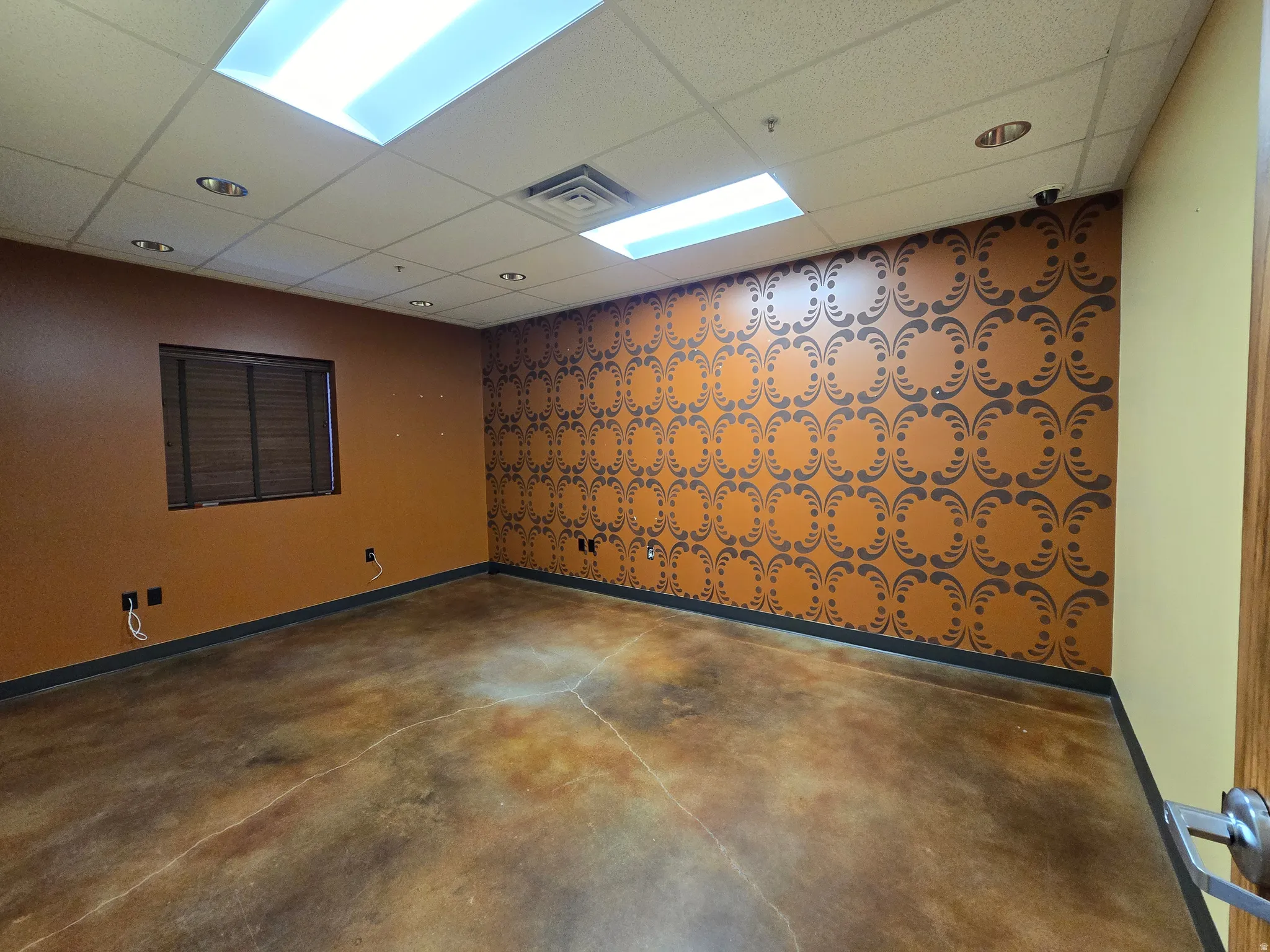 Empty room featuring concrete flooring, a paneled ceiling, wallpapered walls, and an accent wall