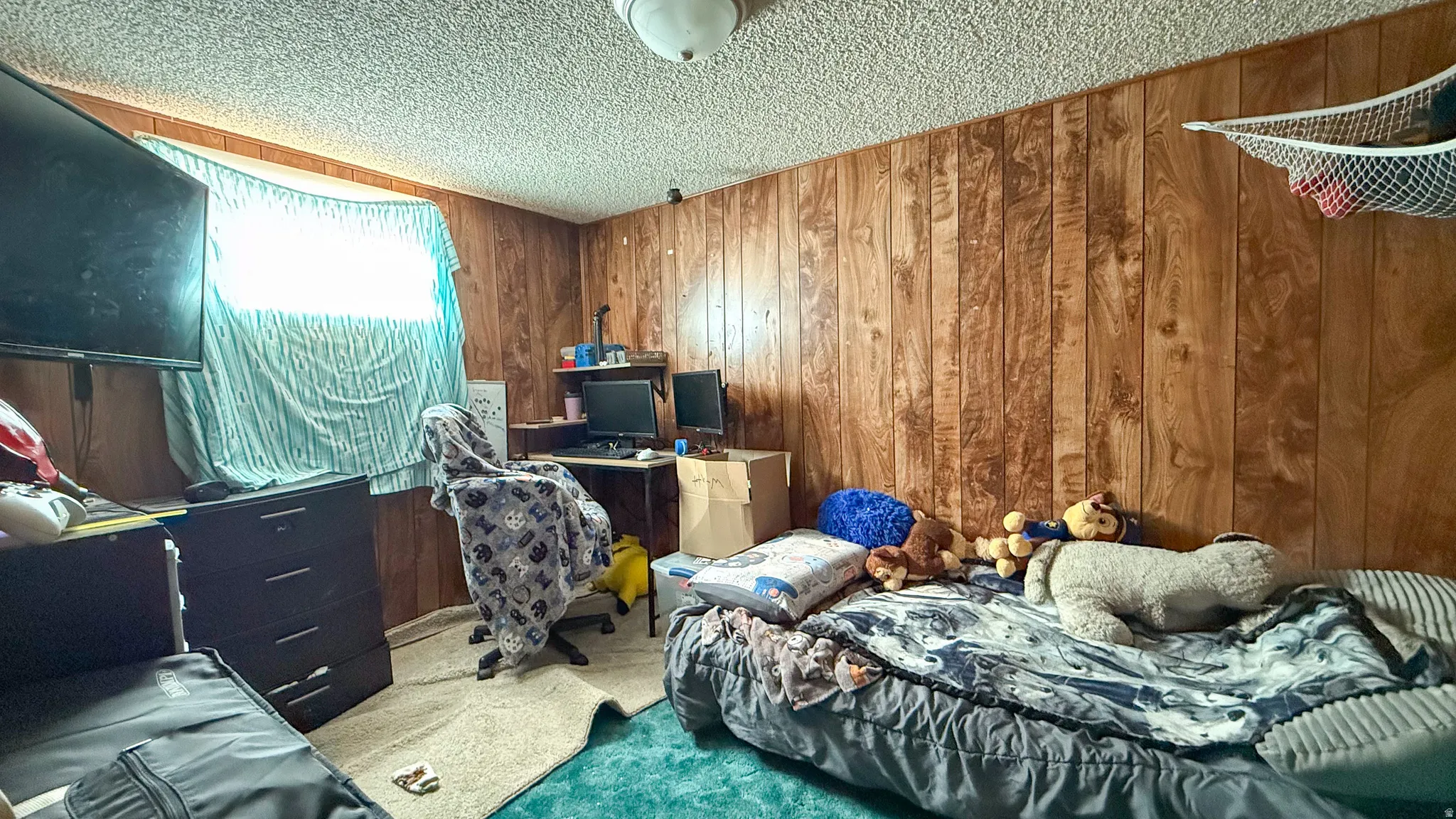 Bedroom with carpet floors, wood walls, a textured ceiling, and a desk