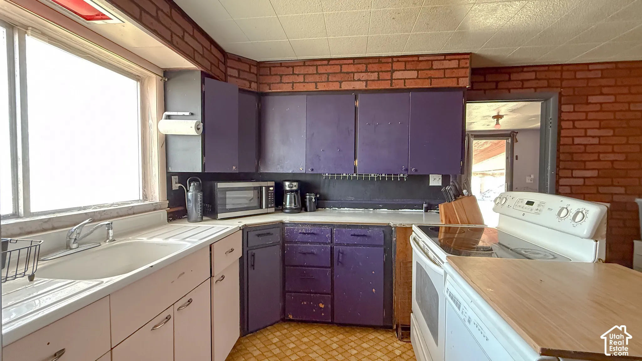 Kitchen with white appliances, light countertops, brick wall, and light flooring