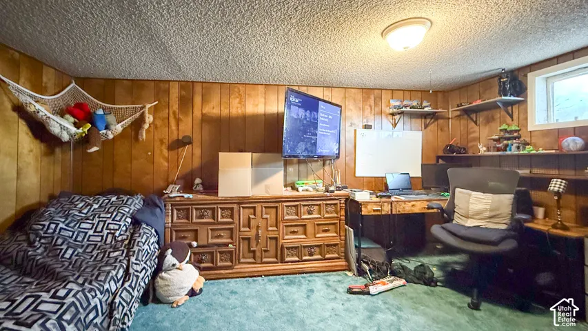 Carpeted bedroom featuring wood walls, a textured ceiling, and an office area