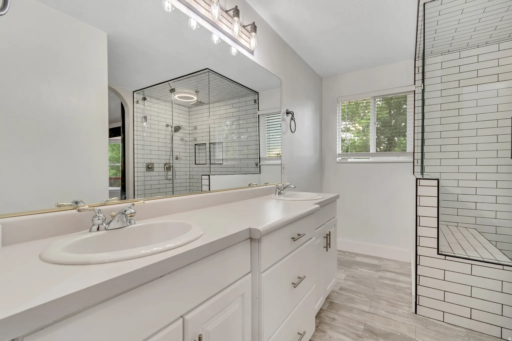 Bathroom featuring a stall shower, double vanity, and light wood-style flooring