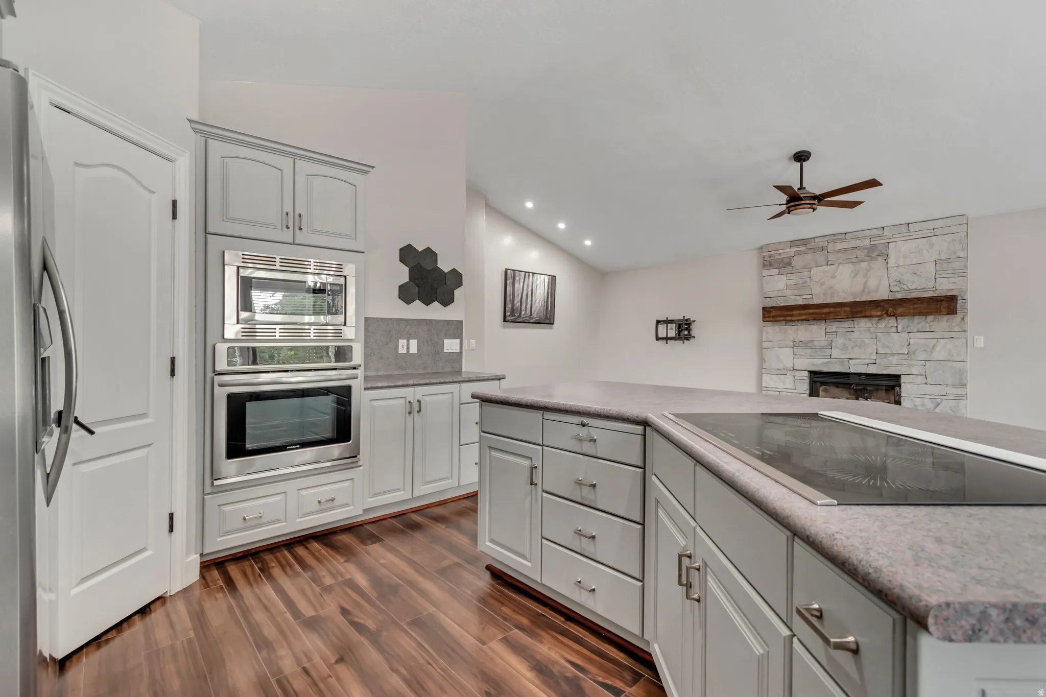 Kitchen with lofted ceiling, stainless steel appliances, a fireplace, gray cabinets, and dark wood-type flooring
