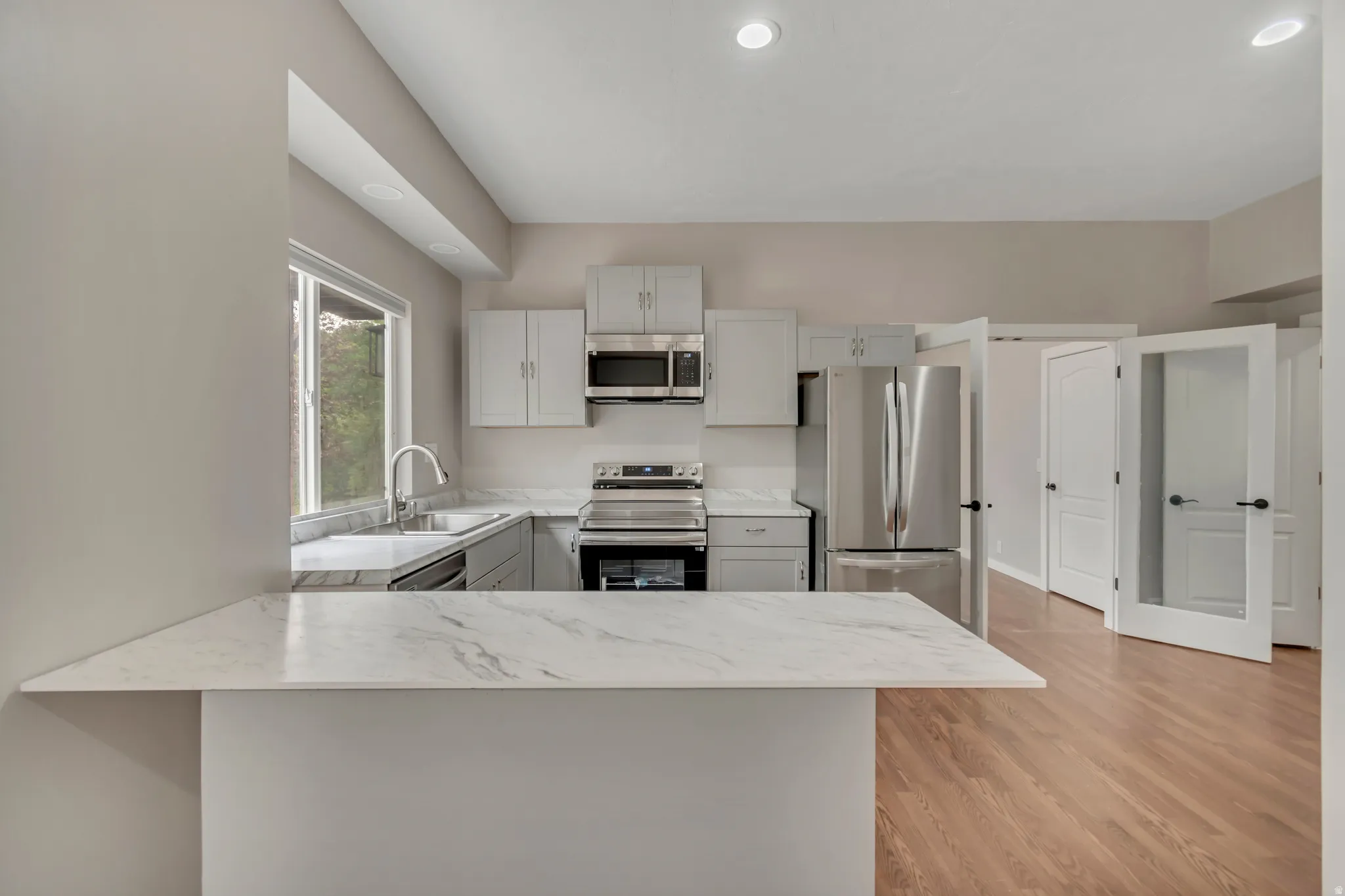 Kitchen with stainless steel appliances, a peninsula, light wood-style flooring, recessed lighting, and light stone counters