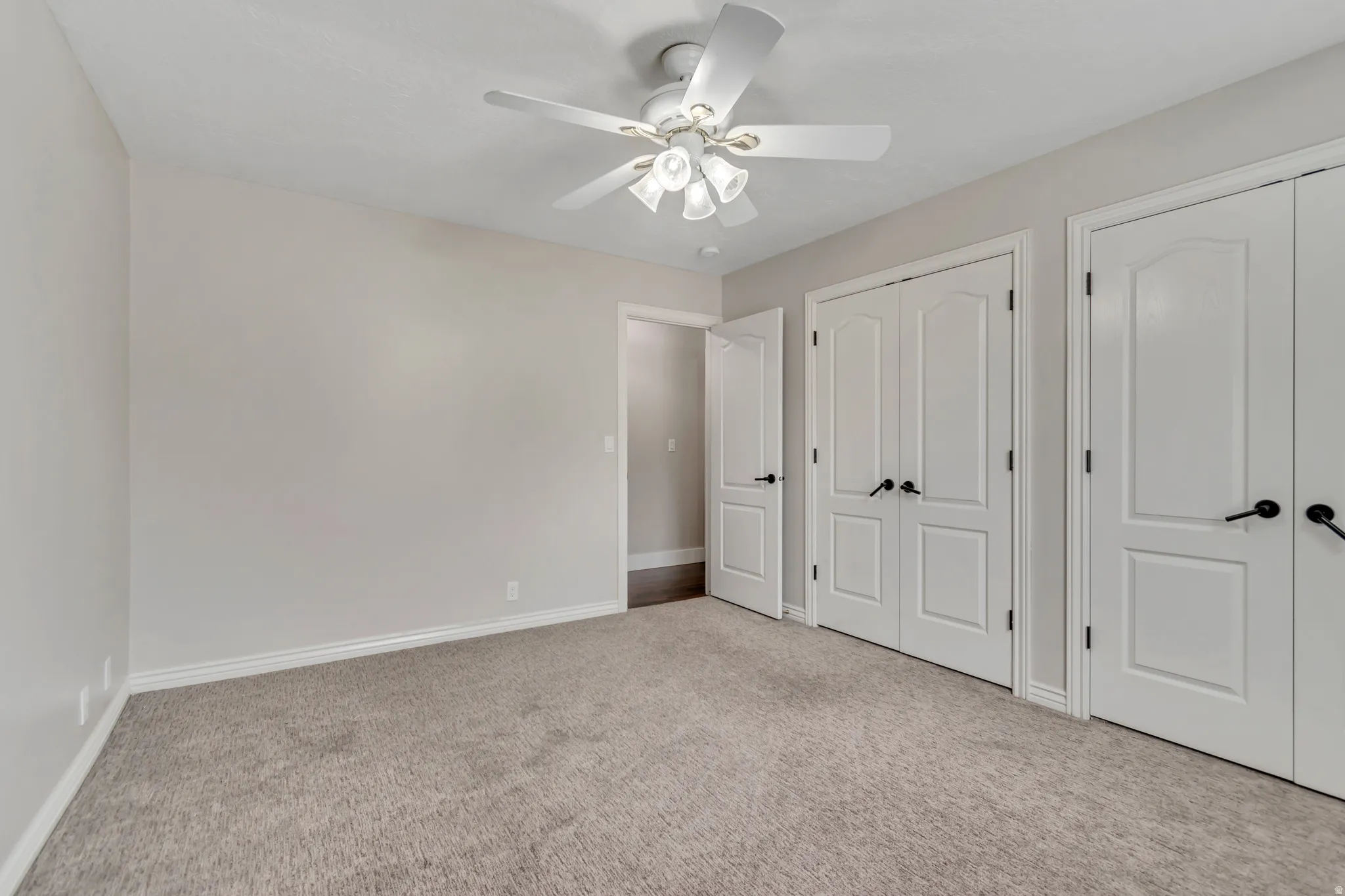 Unfurnished bedroom with two closets, light carpet, and ceiling fan