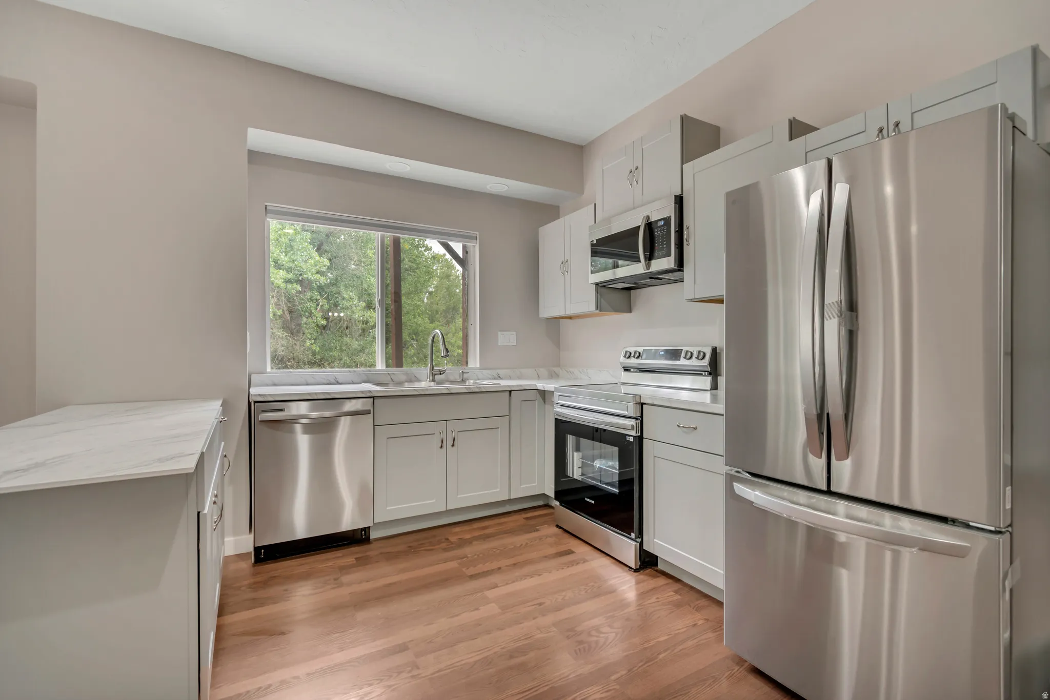 Kitchen with appliances with stainless steel finishes, light wood-style flooring, light stone countertops, white cabinets, and a peninsula