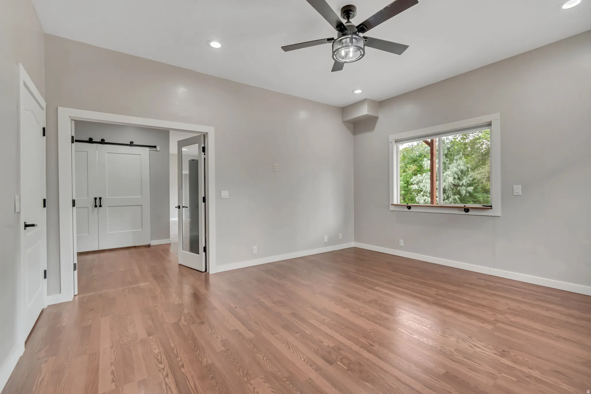 Empty room with a barn door, light wood-style flooring, recessed lighting, and ceiling fan