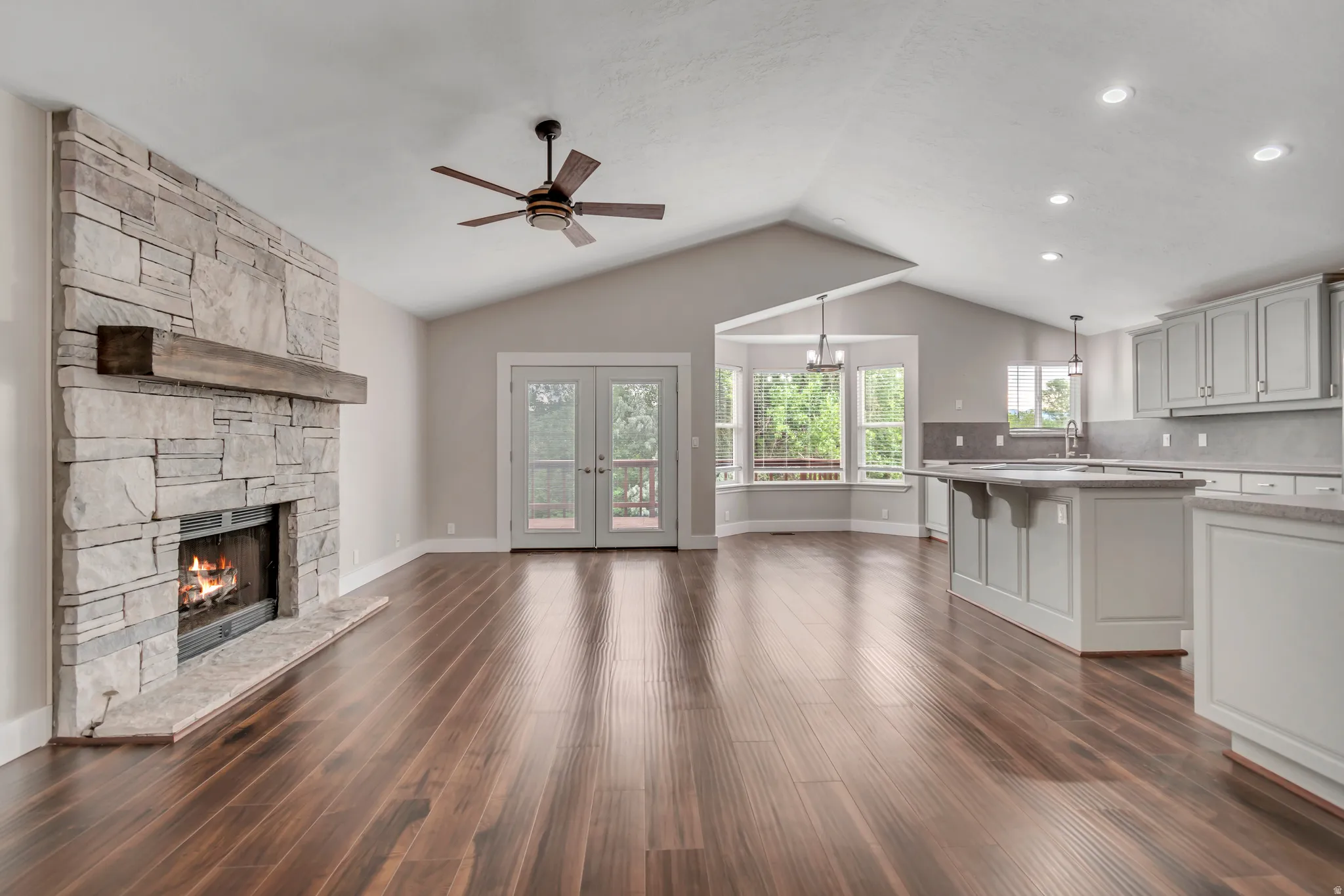 Unfurnished living room with a ceiling fan, a fireplace, dark wood-style flooring, vaulted ceiling, and french doors