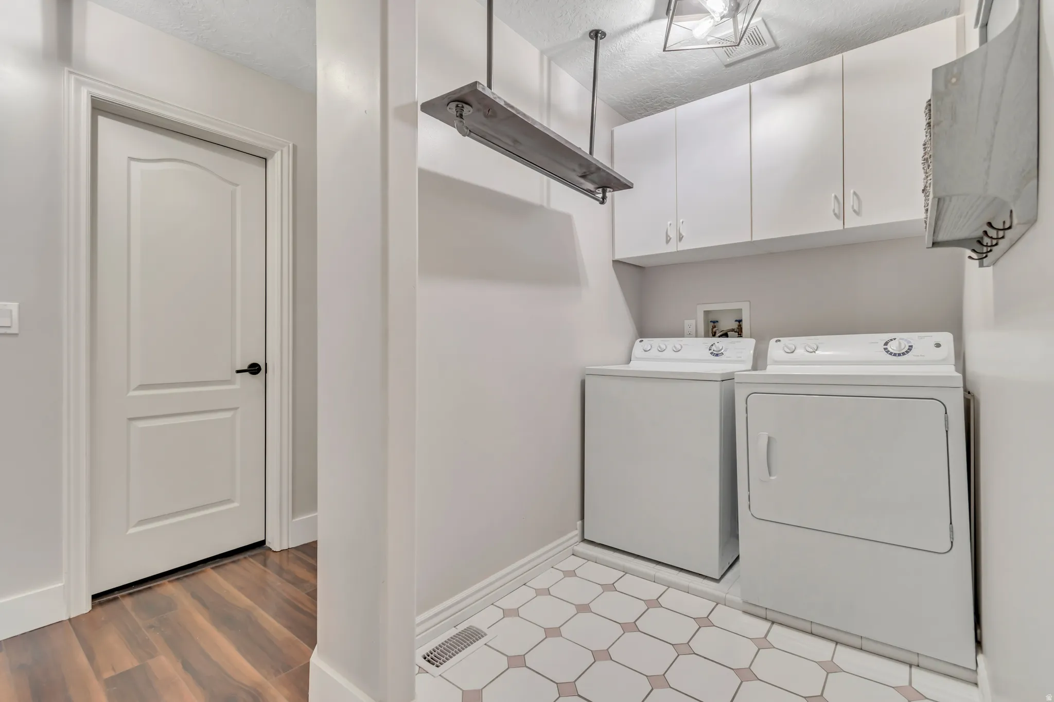 Washroom with a textured ceiling, independent washer and dryer, cabinet space, and light wood-style flooring
