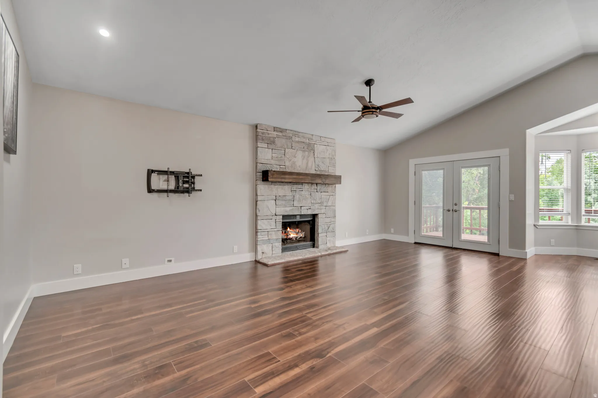 Unfurnished living room with a fireplace, dark wood-style flooring, vaulted ceiling, french doors, and ceiling fan