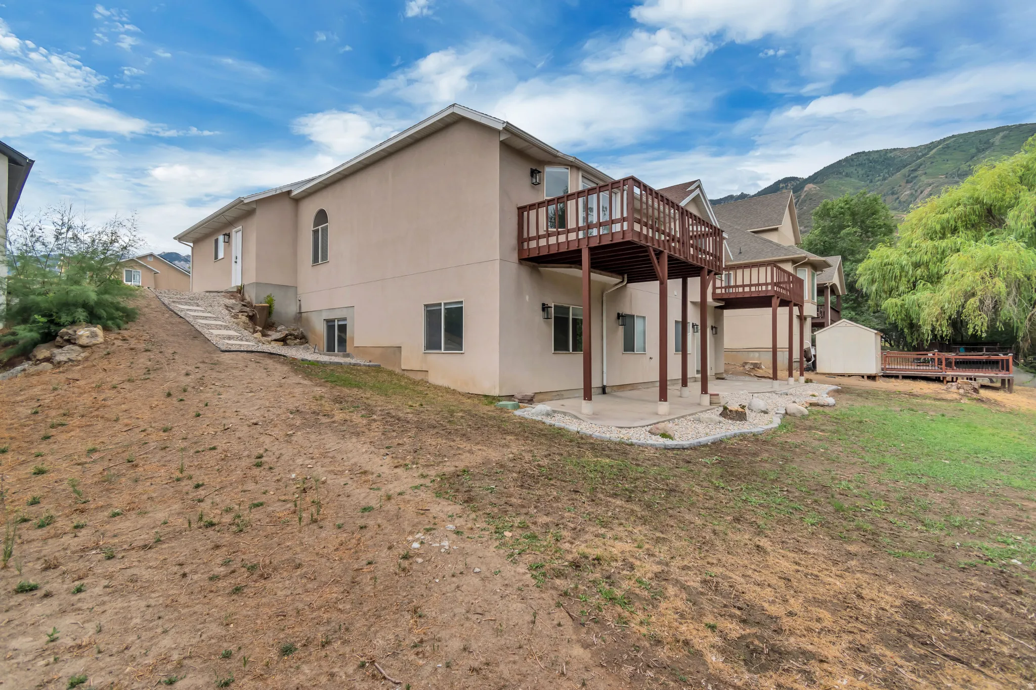 Back of property featuring a patio area, stucco siding, a deck with mountain view, a storage unit, and a lawn