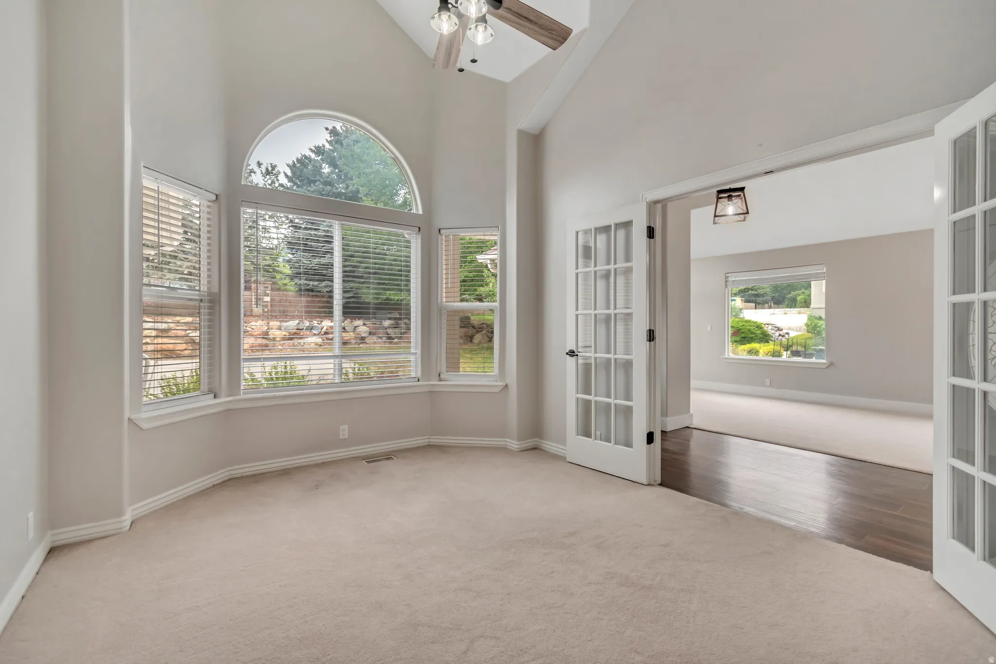 Carpeted empty room with high vaulted ceiling, french doors, and ceiling fan