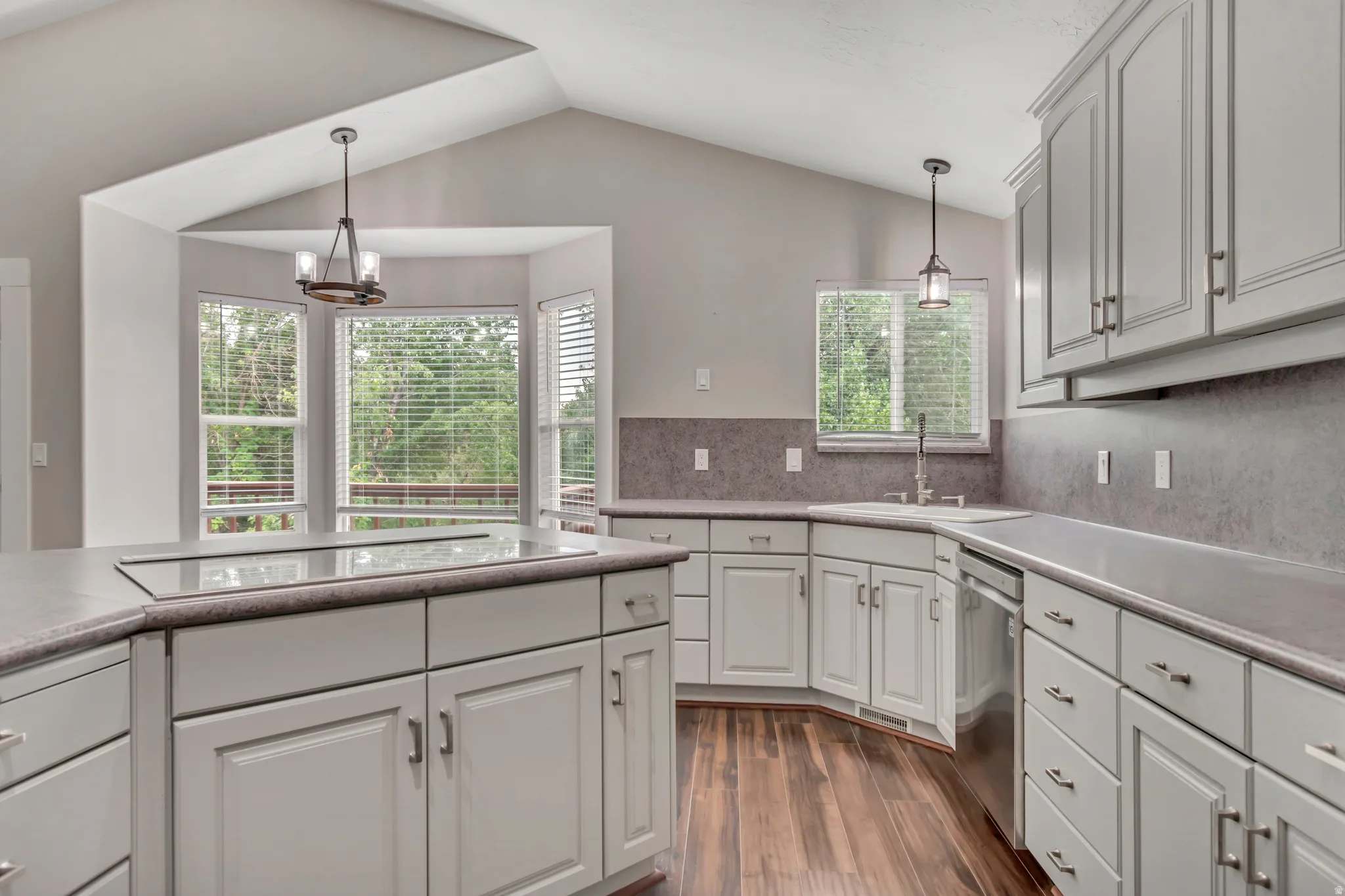 Kitchen with pendant lighting, dark wood-style flooring, light countertops, tasteful backsplash, and vaulted ceiling