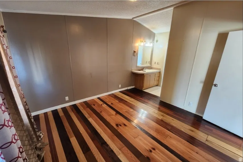 Unfurnished bedroom featuring a textured ceiling, dark wood-type flooring, ensuite bath, and a decorative wall