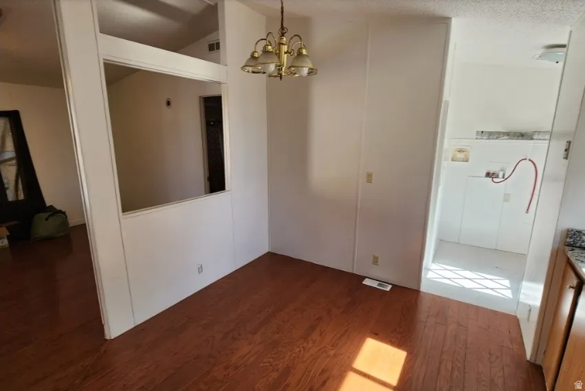 Unfurnished dining area with dark wood-type flooring, a chandelier, and a textured ceiling