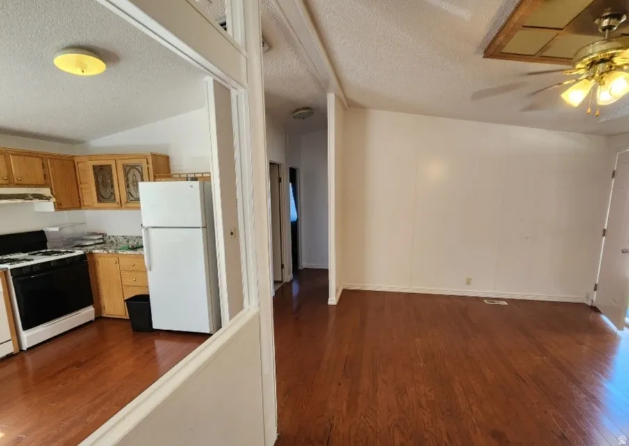 Kitchen with gas range oven, freestanding refrigerator, dark wood-style flooring, light countertops, and a textured ceiling