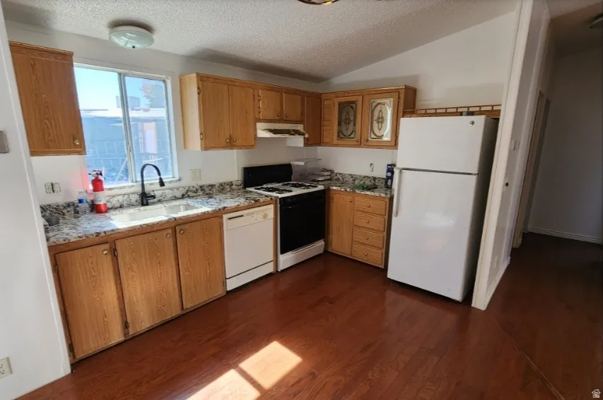 Kitchen with white appliances, dark wood finished floors, a textured ceiling, lofted ceiling, and light stone counters