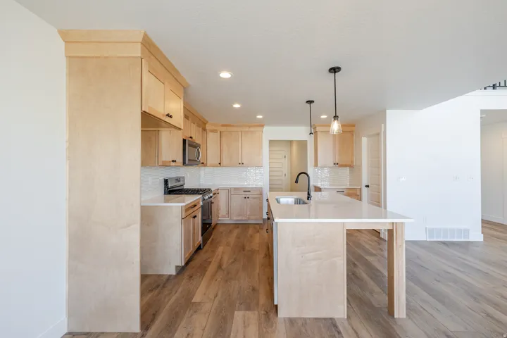 Kitchen with light wood finish cabinetry, stainless steel appliances, light wood finished floors, a kitchen island with sink, and pendant lighting