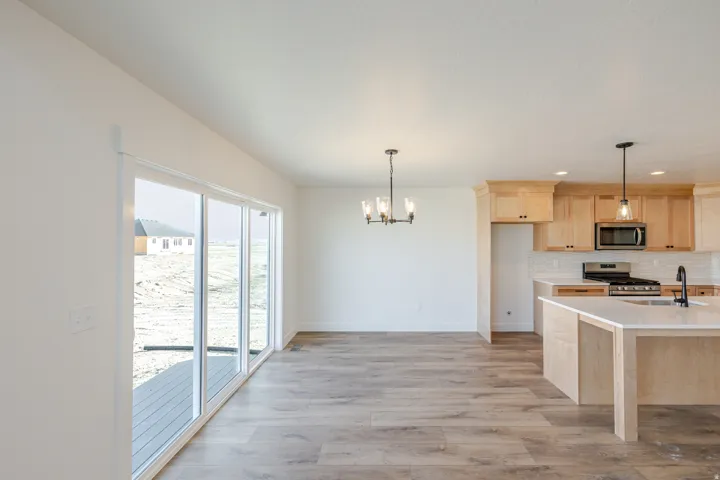 Kitchen with light wood finish cabinetry, a chandelier, light wood-style flooring, stainless steel appliances, and light stone counters