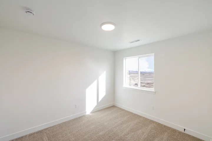 Empty room with light carpet and a smoke detector