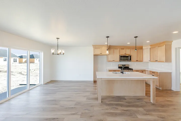 Kitchen featuring light wood finish cabinets, stainless steel appliances, a chandelier, a center island with sink, and light wood finished floors