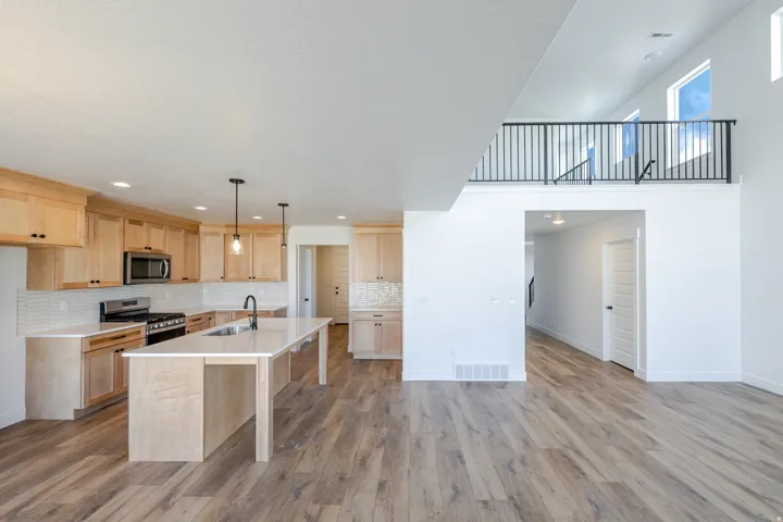 Kitchen with light wood finish cabinetry, stainless steel appliances, a kitchen island with sink, and light wood-style floors