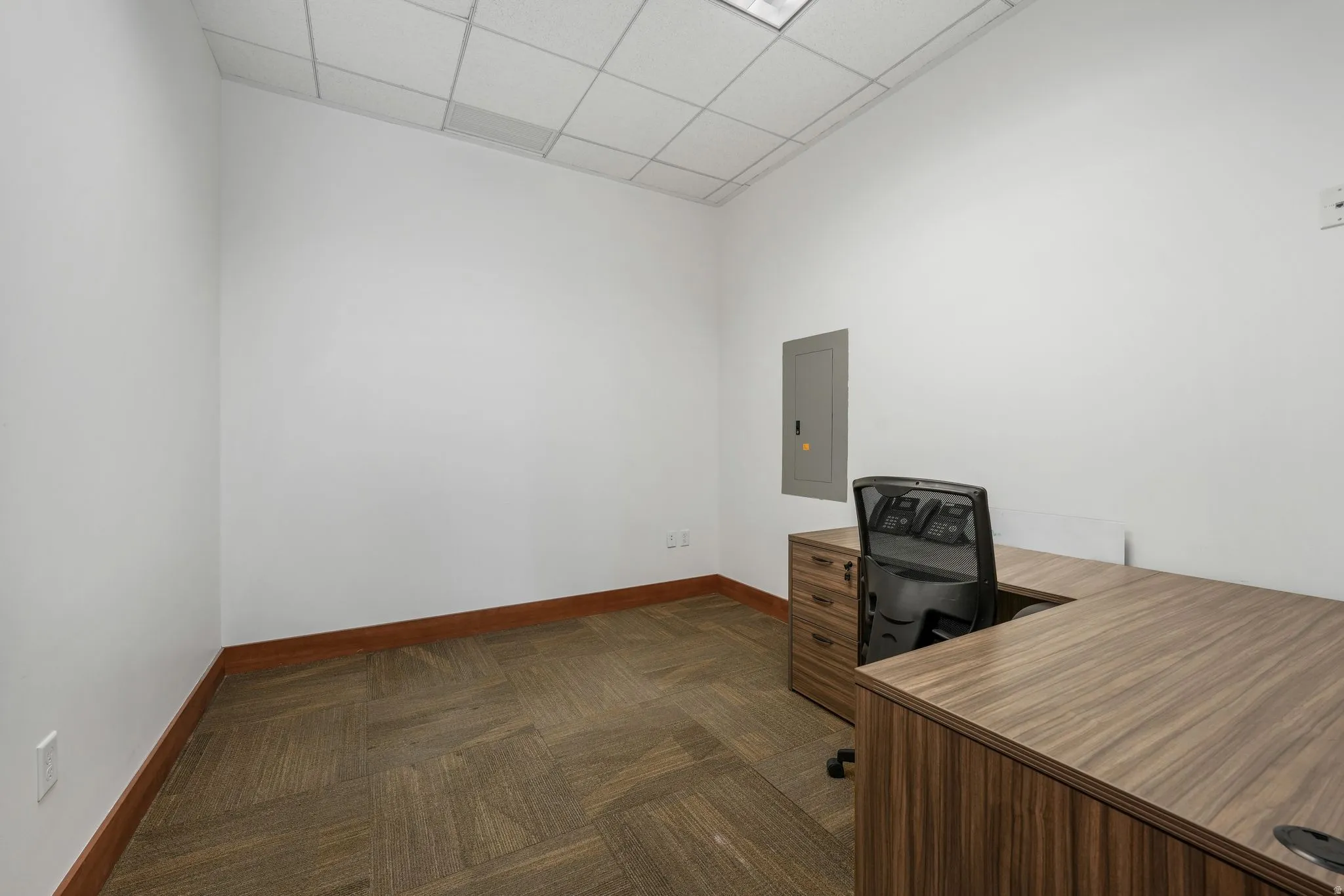 Home office with dark carpet, a drop ceiling, and electric panel
