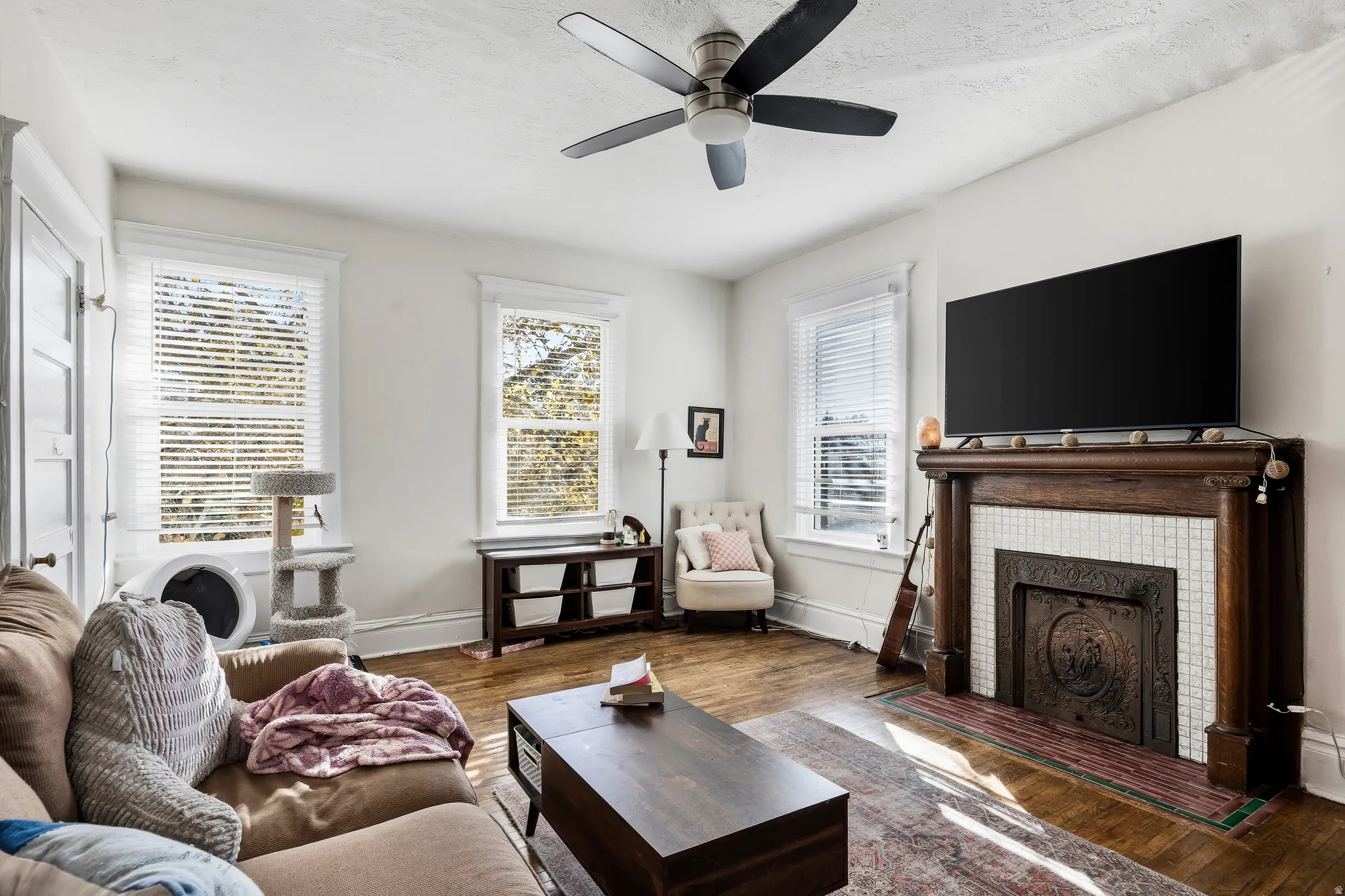 Living room with wood finished floors, a tiled fireplace, a ceiling fan, and a textured ceiling