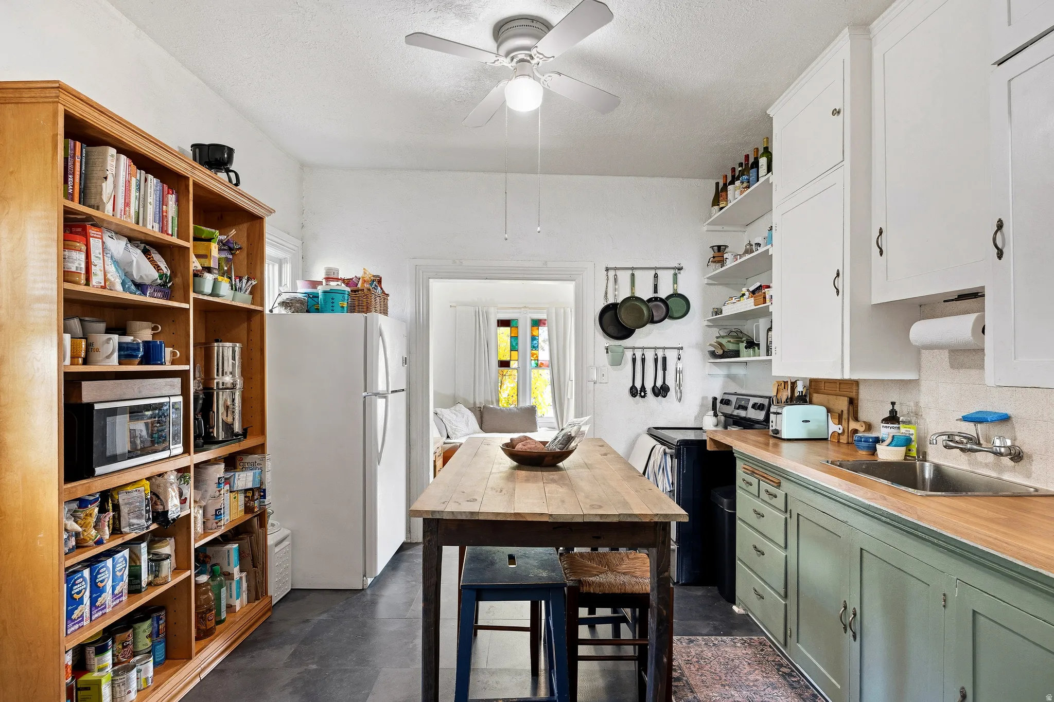 Kitchen with open shelves, freestanding refrigerator, green cabinets, stainless steel microwave, and backsplash