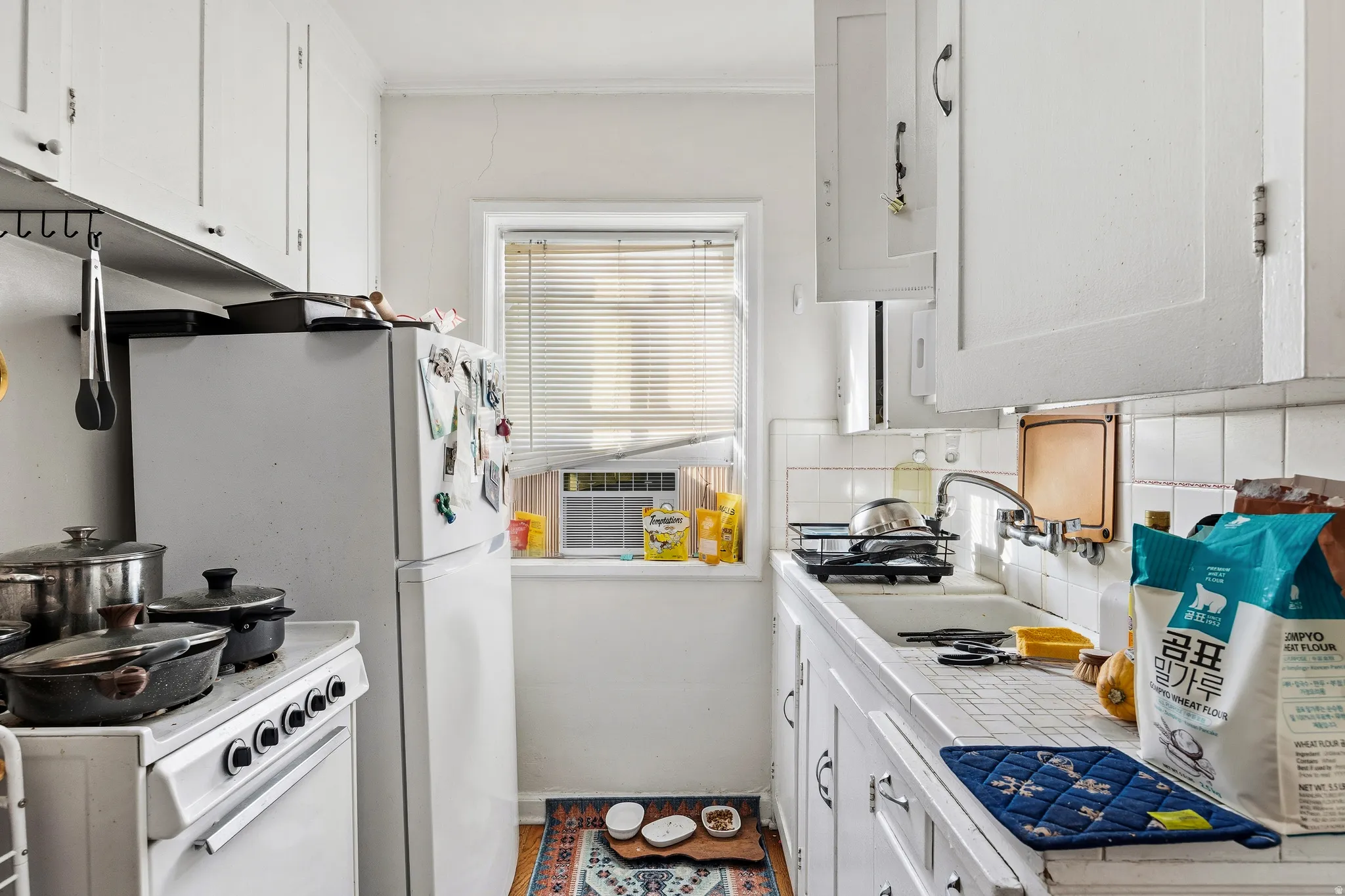 Kitchen featuring tile counters, white cabinetry, tasteful backsplash, white appliances, and crown molding
