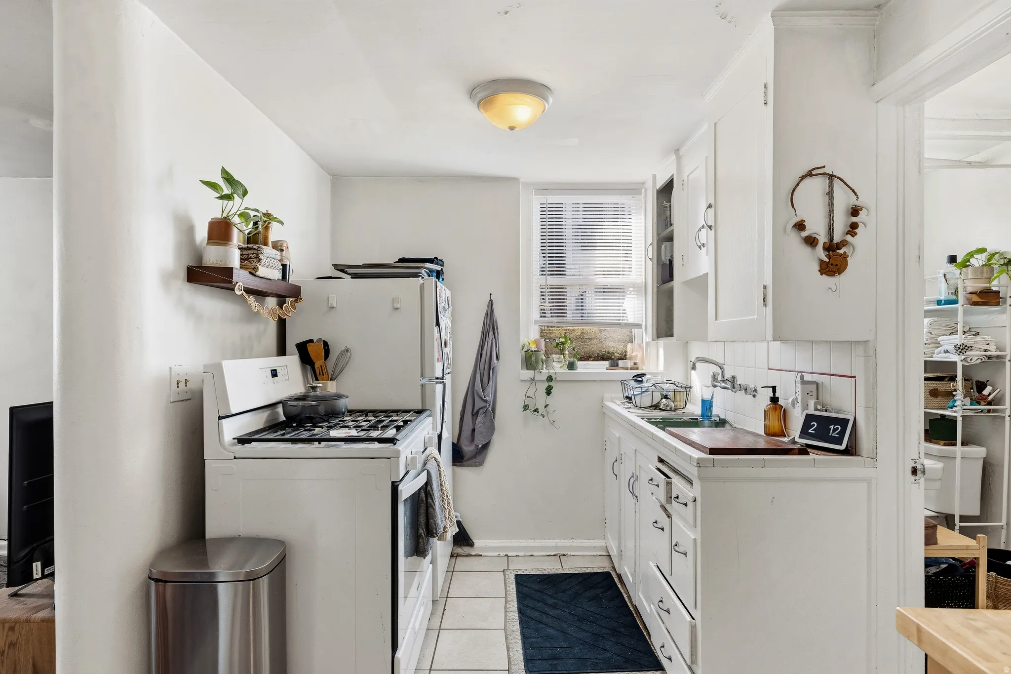 Kitchen with white appliances, white cabinets, tile counters, light tile patterned floors, and open shelves