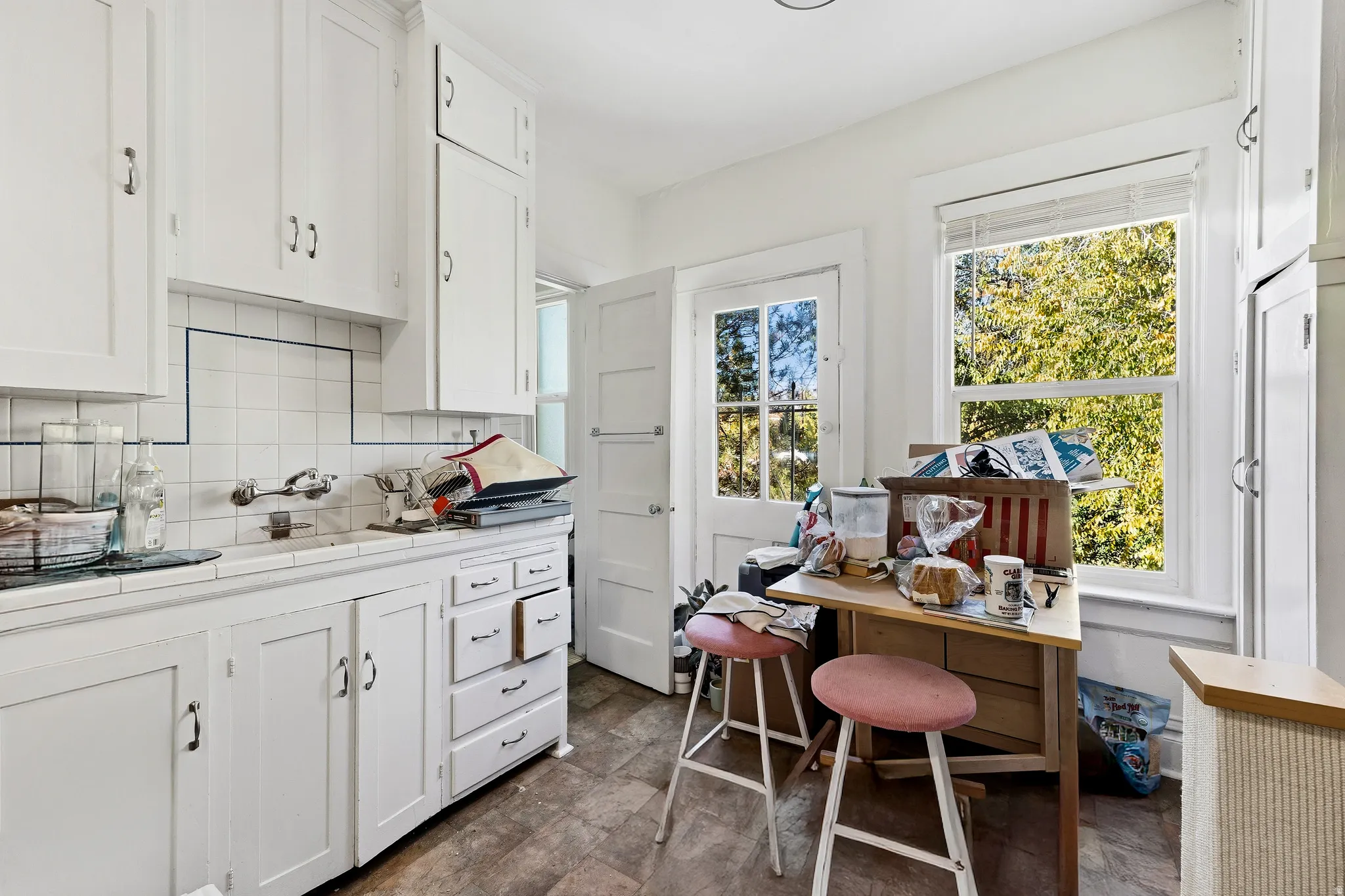 Kitchen with tile counters, white cabinetry, and backsplash