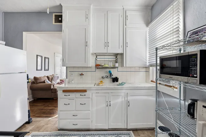 Kitchen featuring tile countertops, white cabinets, freestanding refrigerator, and healthy amount of natural light