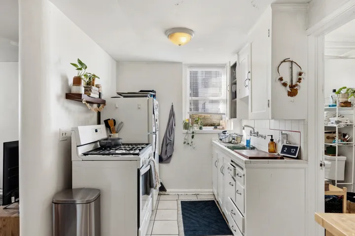 Kitchen with white appliances, white cabinets, tile counters, light tile patterned floors, and open shelves