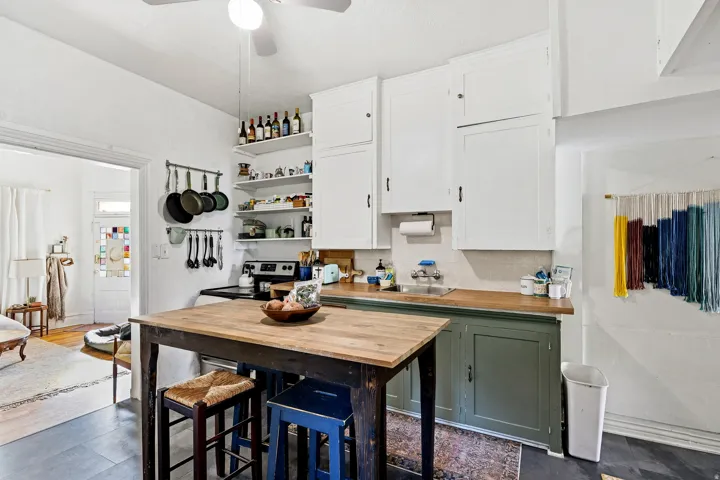 Kitchen with open shelves, white cabinetry, green cabinetry, butcher block counters, and stainless steel range with electric stovetop