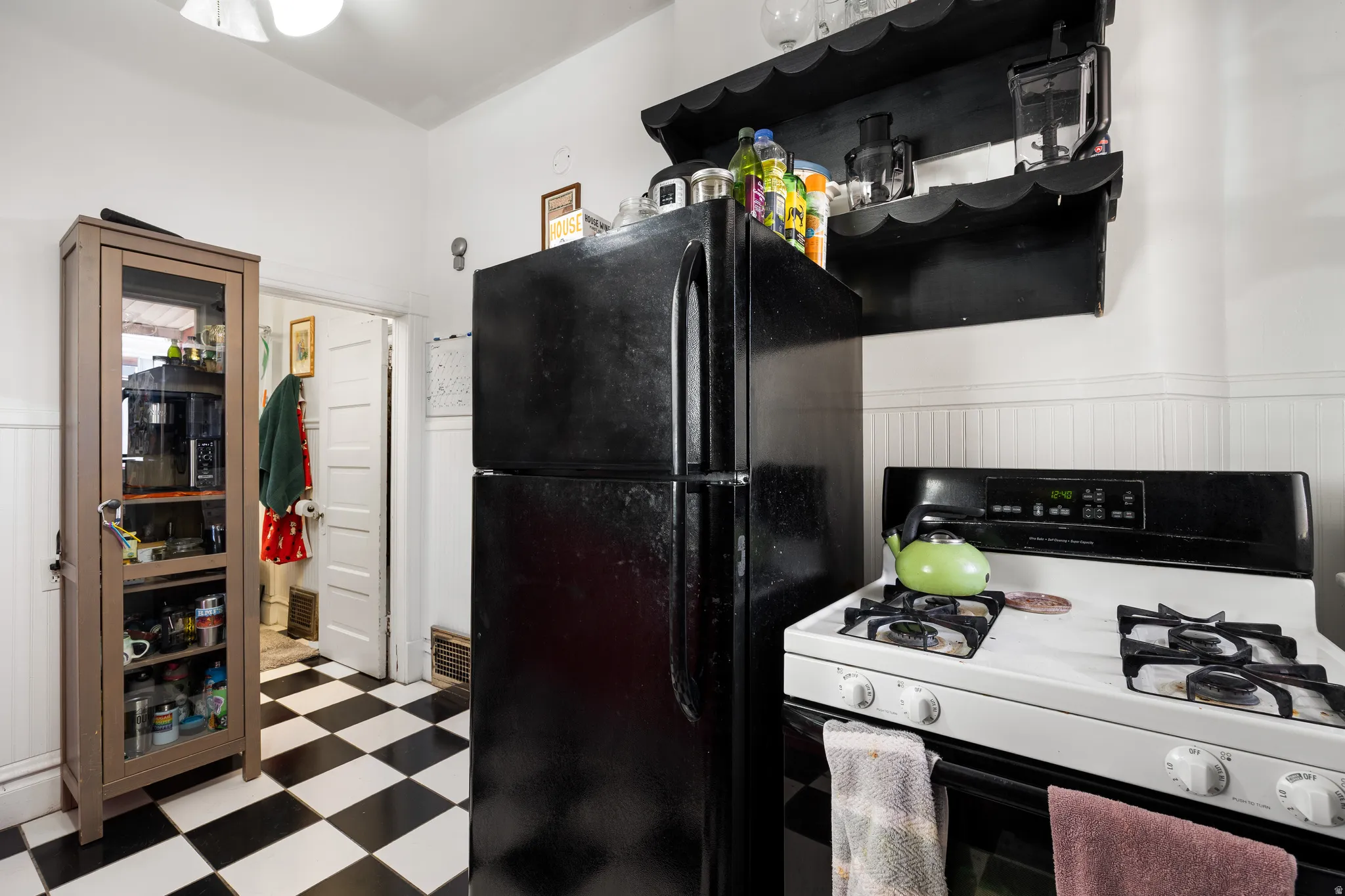 Kitchen with white gas range, tile patterned floors, freestanding refrigerator, and wainscoting