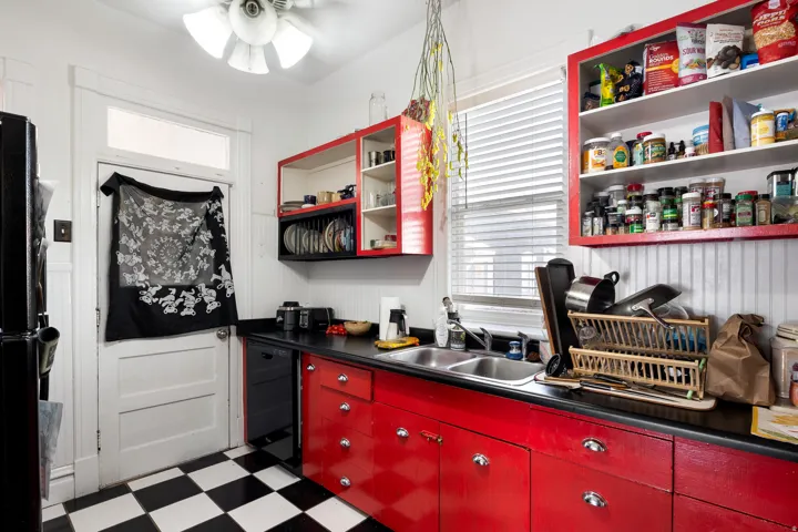 Kitchen with red cabinetry, dark floors, dark countertops, black appliances, and a ceiling fan