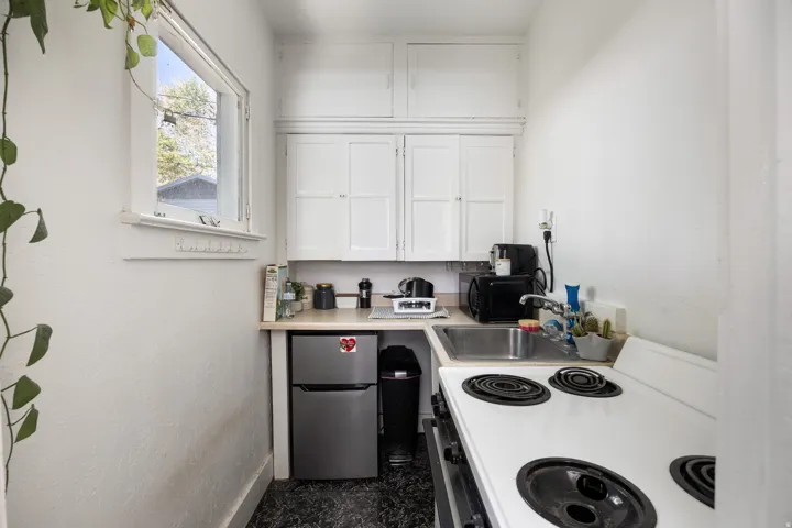 Kitchen featuring white range with electric stovetop, white cabinets, light countertops, freestanding refrigerator, and black microwave