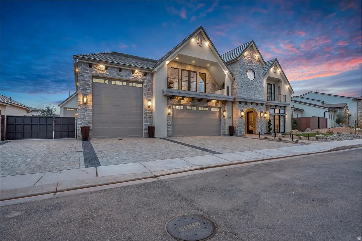 View of front of home with a balcony, stone siding, decorative driveway, and an attached garage