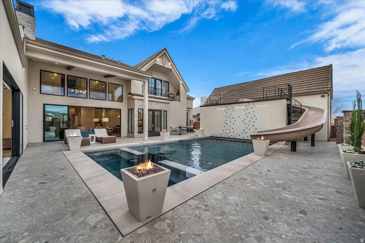 Combined pool / hot tub featuring a water slide, a patio, and an outdoor living space with a fire pit
