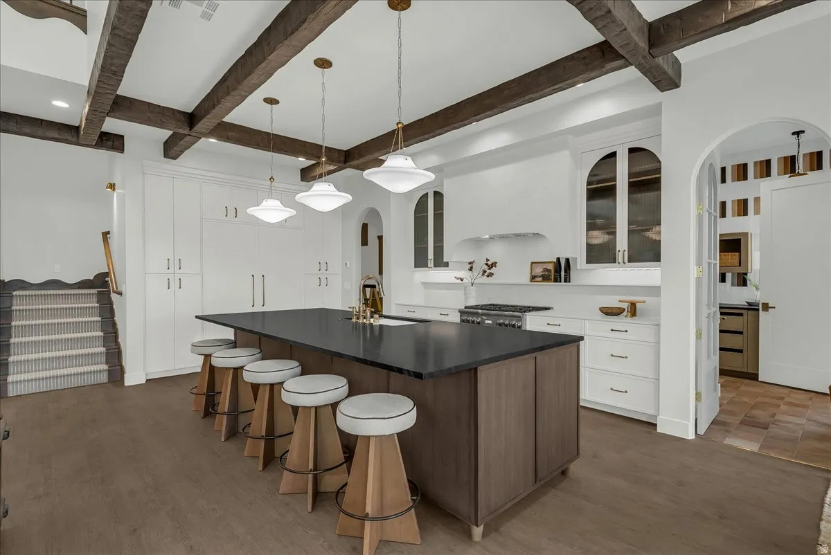 Kitchen featuring glass insert cabinets, arched walkways, an island with sink, a breakfast bar area, and pendant lighting