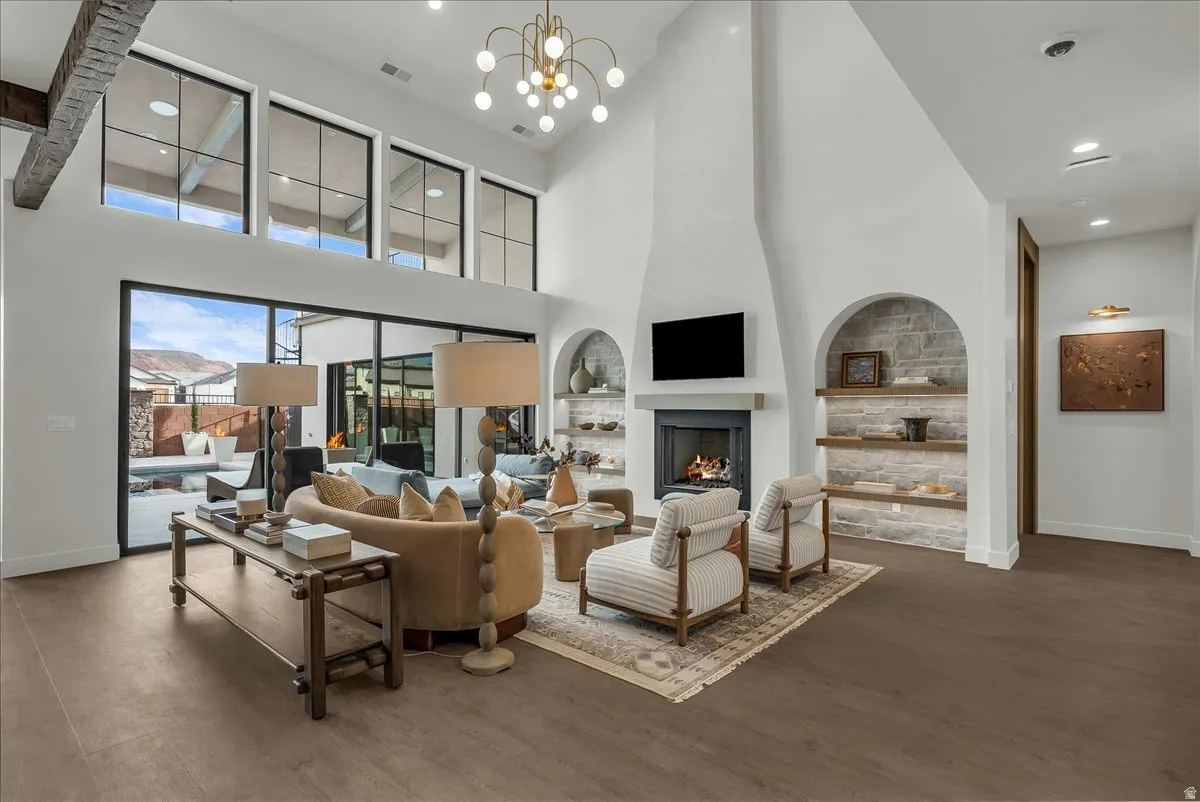Living area with built in features, hanging lights, dark wood-style flooring, a large fireplace, and a high ceiling
