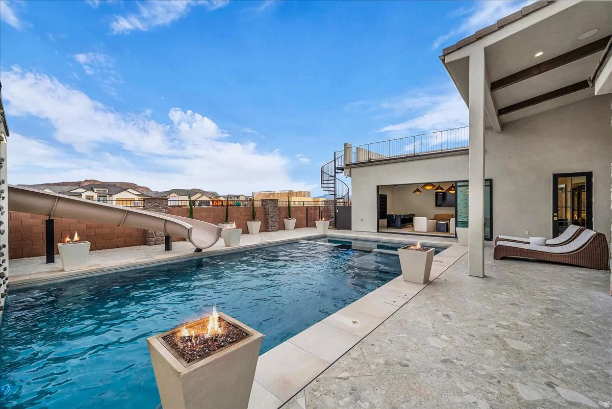 View of swimming pool with an outdoor fire pit, a water slide, patio surround, a fenced backyard, and a residential view
