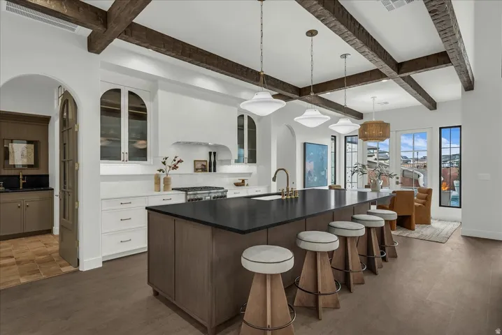 Two tone kitchen with a kitchen island with sink, glass fronted cabinets, a breakfast bar area, arched walkways, and hanging light fixtures